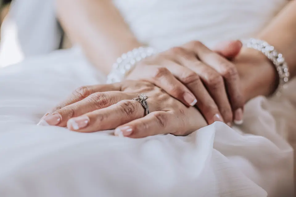 Handen met een ring en een armband op een witte jurk
